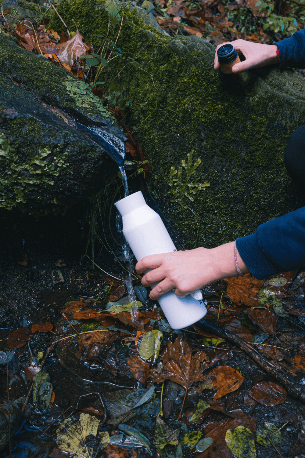 Man replenishing water bottle from natural spring, promoting eco-friendly hydration and preservation of natural resources.