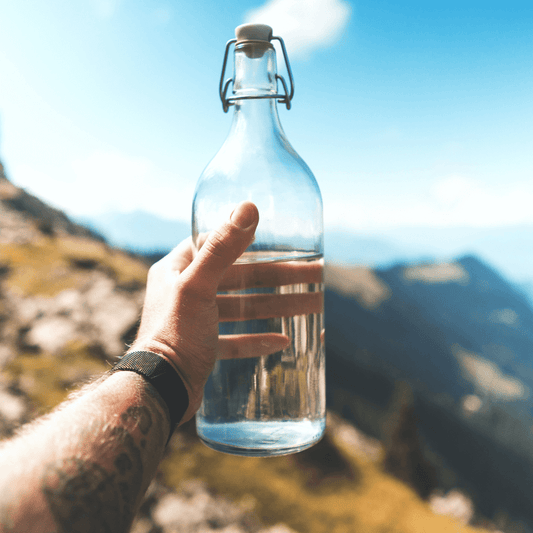 A refreshing image of a clear bottle filled with crystal-clear mountain water surrounded by lush green nature, the perfect drink for outdoor enthusiasts