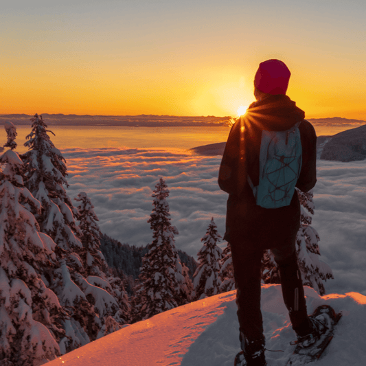 Snowshoe hiker standing on a mountain enjoying the sunset, with a beautiful winter landscape in the background