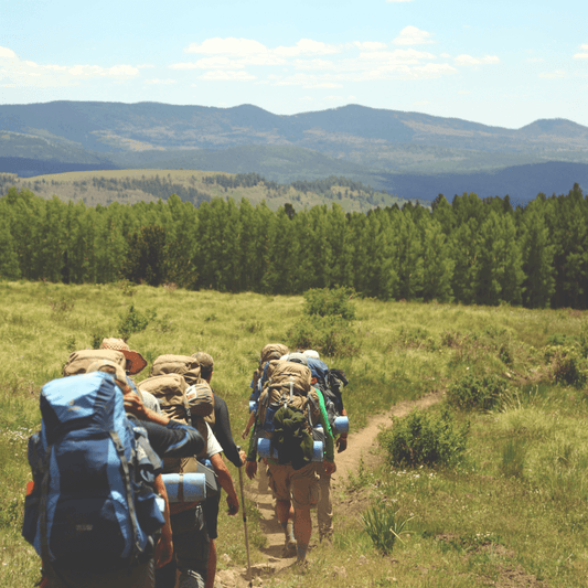 Group of hikers walking through an open range in the sun with hills in the background. Enjoying the beauty of nature on a hiking adventure.