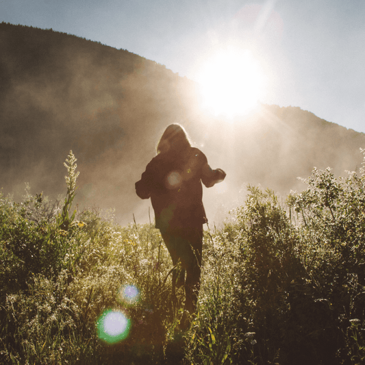 Woman standing in the sun on a field, wearing hiking gear and holding a first aid kit. 