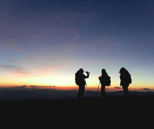 Three hikers enjoying a scenic sunset on their outdoor adventure